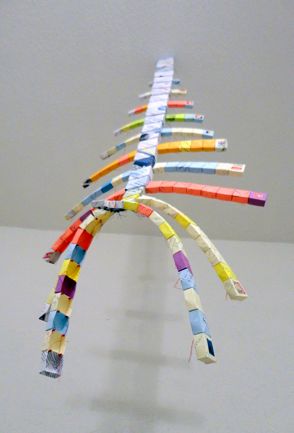 A long vertical paper sculpture with arm-like extensions, hung from the ceiling.