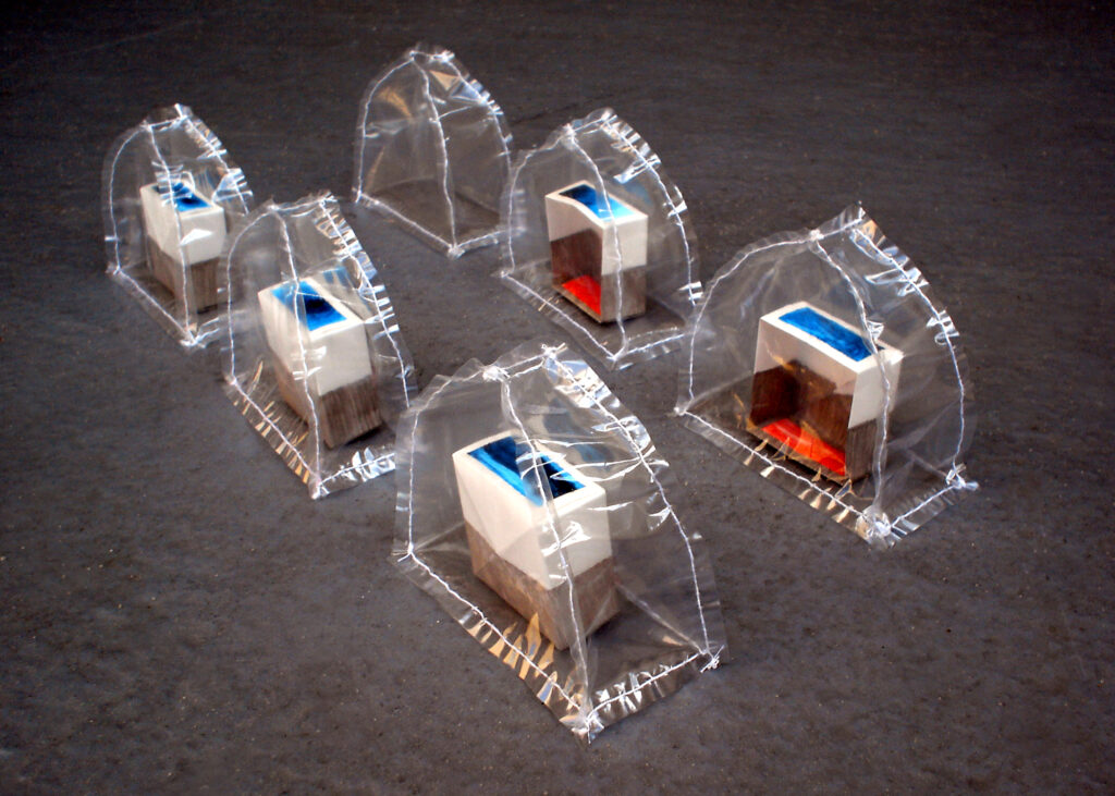 Two rows of clear plastic domes with paper boxes inside. Each box has a blue painting on top, and a red painting inside.