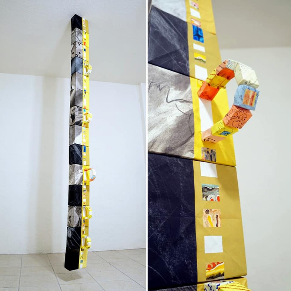 A long, narrow, vertical sculpture hung from the ceiling by artist Joanna White.