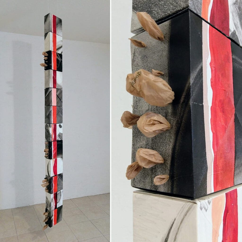 A long, narrow, vertical sculpture hung from the ceiling with a red and pink oil painting down the front.