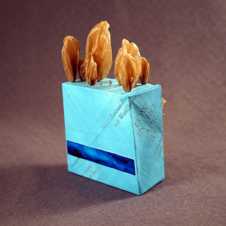 A blue paper origami box with a narrow blue oil painting and tufts of brown plastic grocery bag sprouting out of the top.