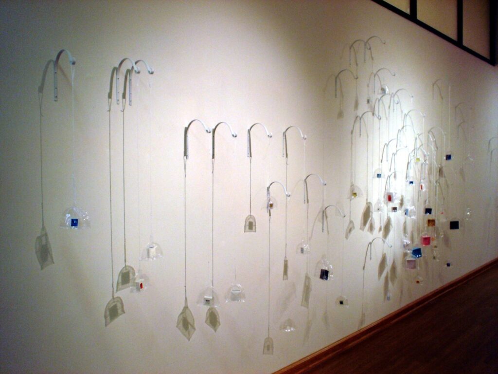An installation with small paper boxes enclosed in plastic domes and suspended from the wall.