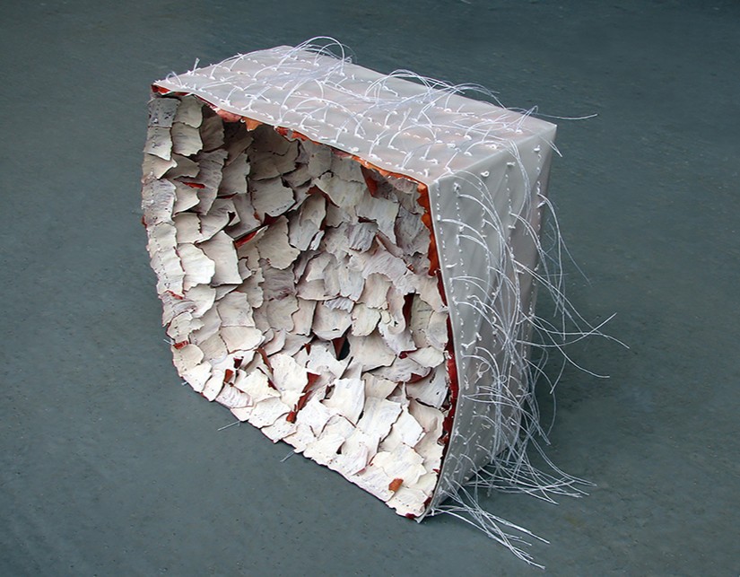 A tissue paper box filled with purple onion skins painted white, with long threads extending out from each stitched skin.