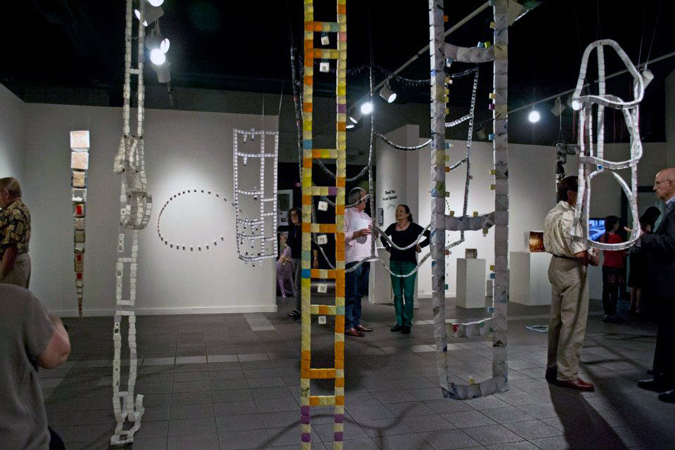An installation view of many paper sculptures hanging vertically from the ceiling.