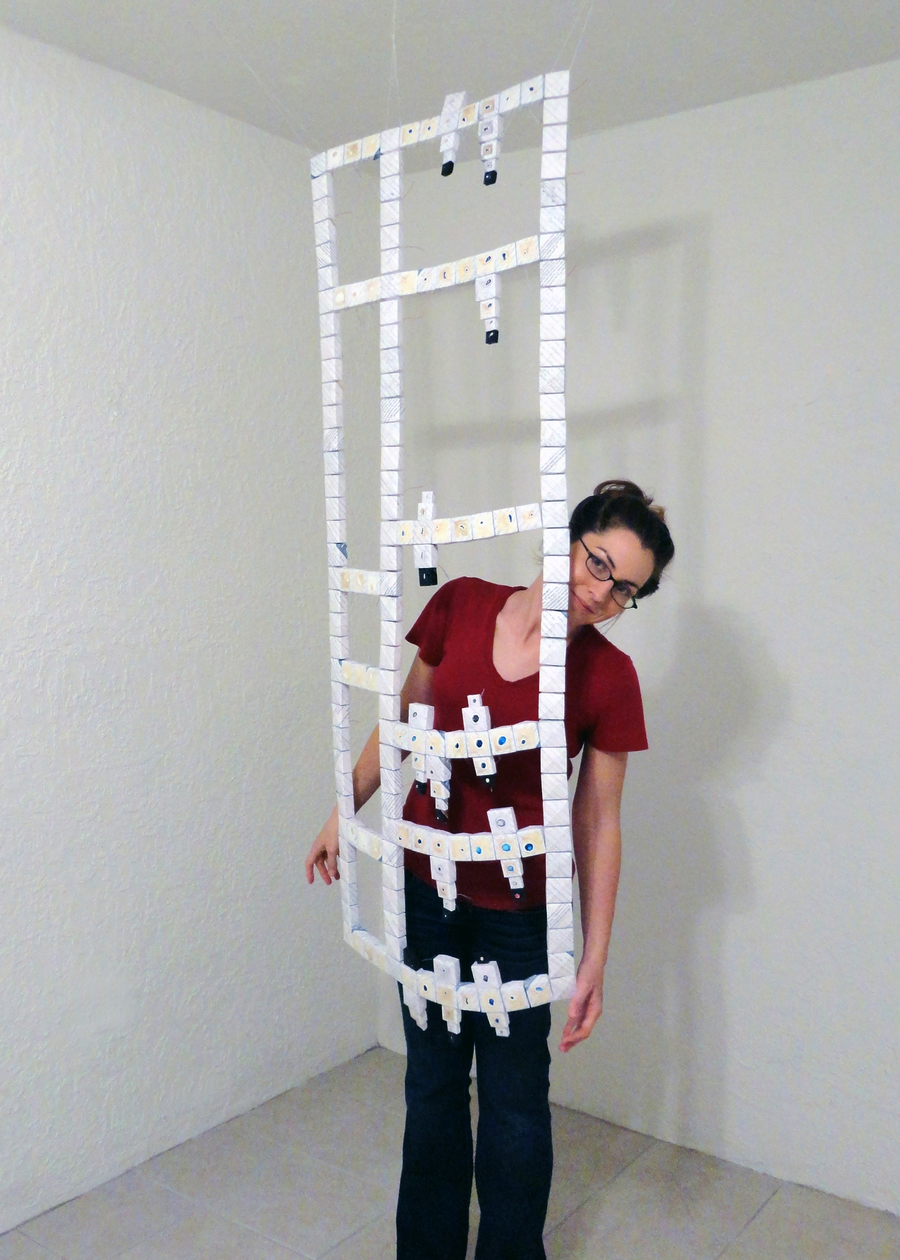 Artist Joanna White standing behind a grid-like paper sculpture hung from the ceiling.