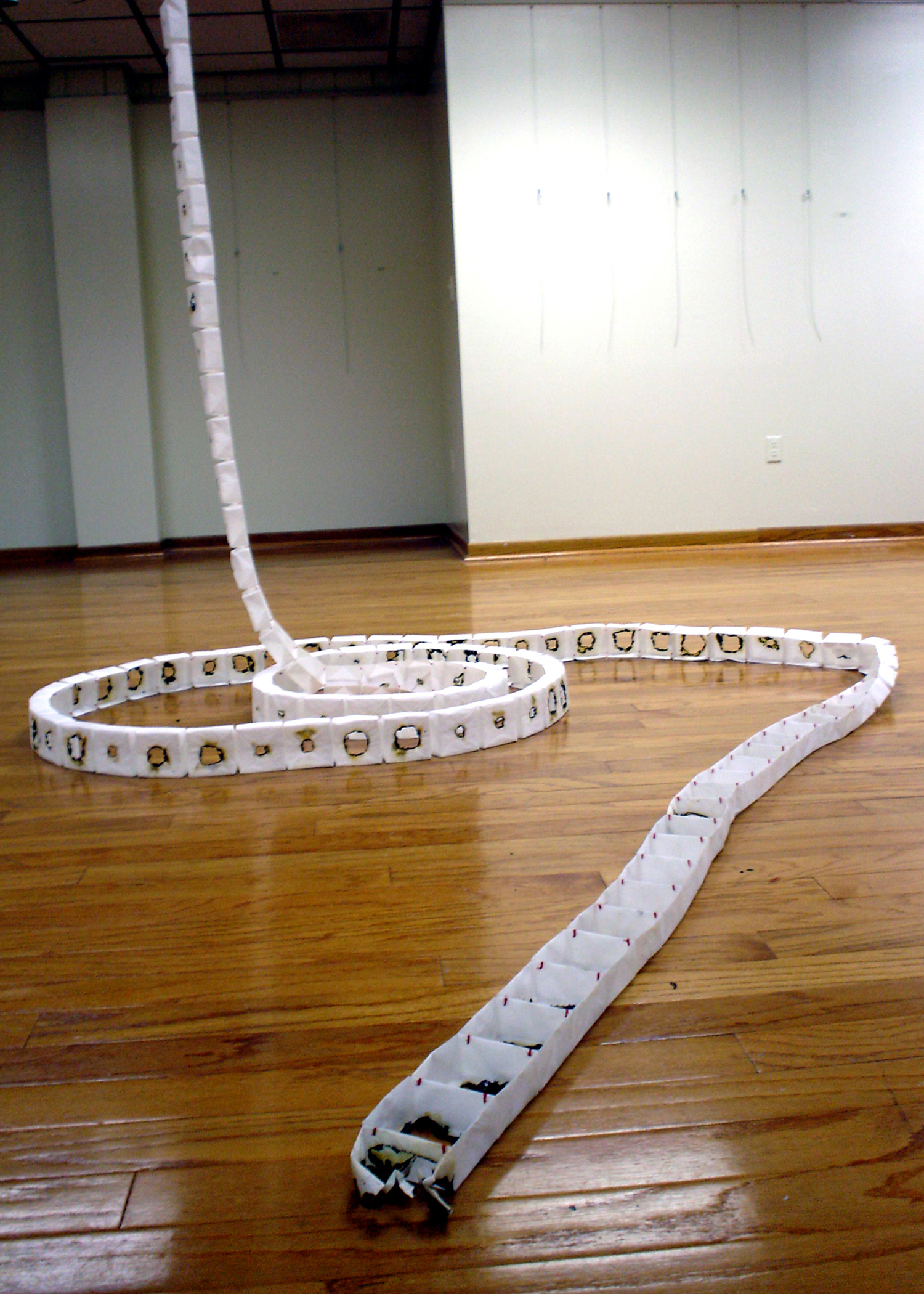A string of tracing paper boxes by artist Joanna White, hanging vertically from the ceiling and forming a spiral on the gallery floor.