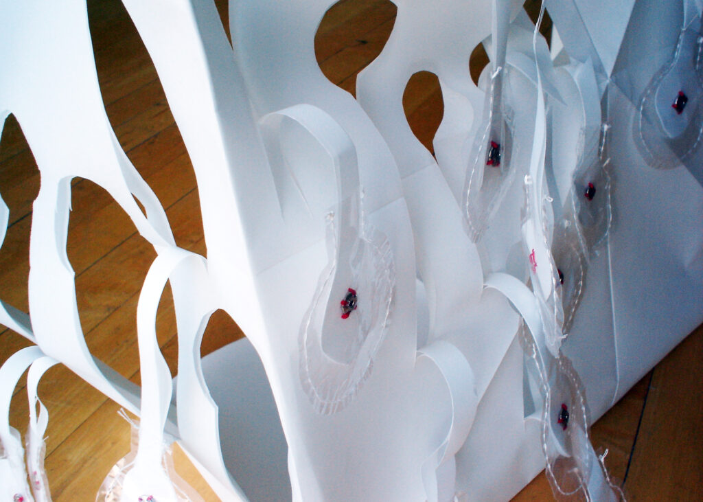 Detail view of paper sculpture titled Ache, by artist Joanna White, showing the cut-out tabs with sewn-on metal garment snaps.