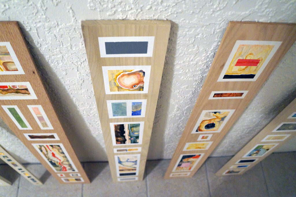 An overhead view of a row of narrow wooden boards with segmented oil paintings applied to the fronts by artist Joanna White.