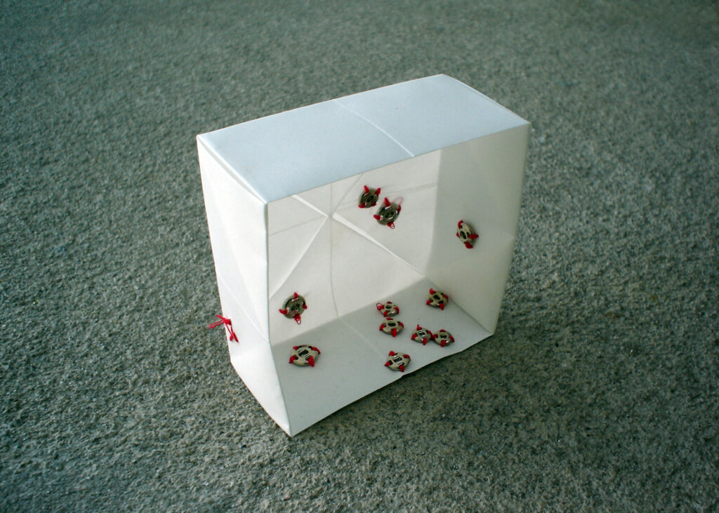 A small white paper box with metal garment snaps stitched to the inside with red thread, by artist Joanna White.